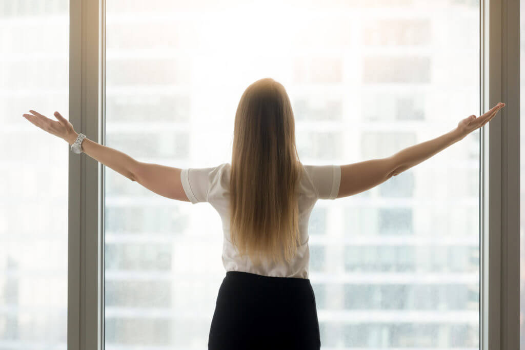 A woman standing in front of a window with her arms outstretched.